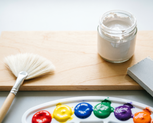 Wood painting supplies including a birch panel, gesso, sandpaper, and acrylic paints on a desk.
